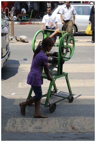 A young girl pushing a laundry mangle along the street